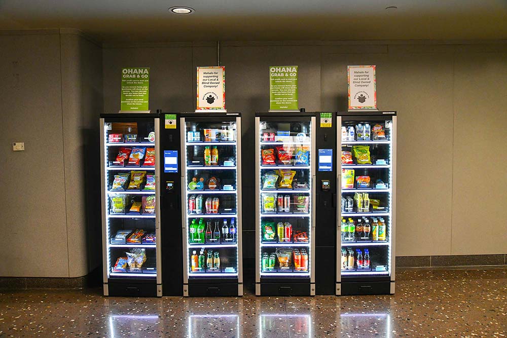 A bank of Blind Vendors Ohana vending machines stocked with snacks and cold drinks at Daniel K. Inouye International Airport.